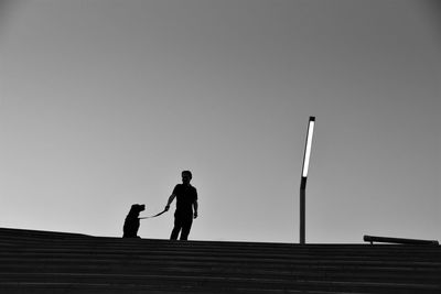 Low angle view silhouette man with dog standing against sky