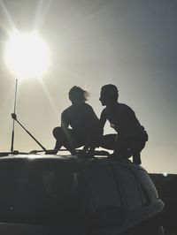 Silhouette man sitting on car against sky