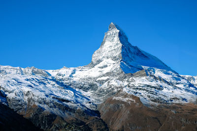 Low angle view of snowcapped mountains against clear blue sky