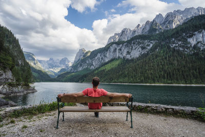 Man sitting on bench by lake against mountains