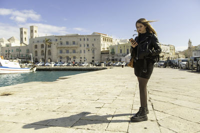 Full length portrait of woman standing in city against sky