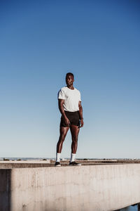 Thoughtful sportsman standing on wall against blue clear sky