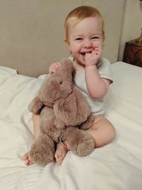 Portrait of cute baby girl with toy sitting on bed at home