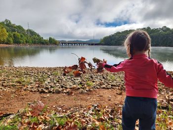 Child throwing autumn leaves near lake