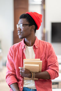 Young happy african american man university teacher sitting in classroom holding pile of books