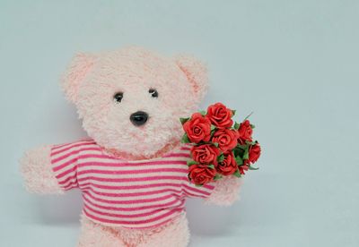 Close-up of teddy bear with artificial roses against gray background