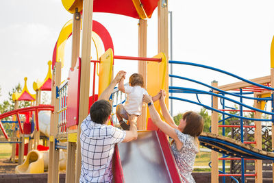 Rear view of people on swing in playground