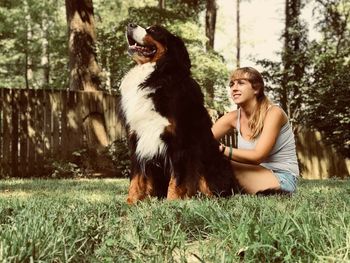 Smiling young woman with dog sitting on grassy field