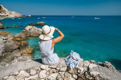 Woman on rock by sea against sky