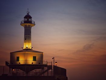 Low angle view of lighthouse by building against sky during sunset