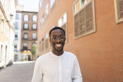 Young man in eyeglasses smiling in front of buildings