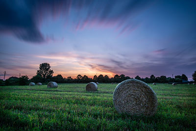 Hay bales on field against sky during sunset