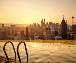Infinity pool against buildings in city during sunset