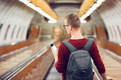 Rear view of young man using mobile phone while standing on escalator