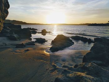 Rocks on beach against sky during sunset