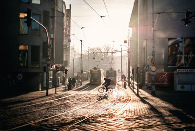 Man riding bicycle on railroad track against train amidst building in city