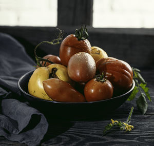 Multicolored tomatoes of different sizes and types in a dark dish and rustic background