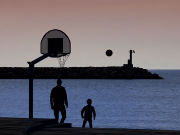 Rear view of silhouette people on basketball hoop against sky