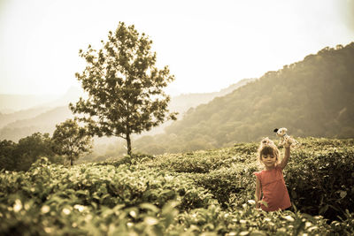 Girl with toy amidst plants on field against sky