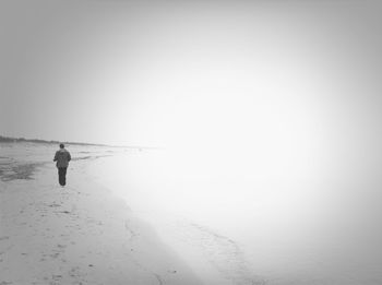 Rear view of person walking on beach against clear sky