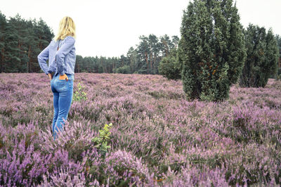 Woman with hands in pockets standing on field against sky