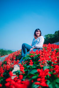 Smiling young woman with flowers on field against sky