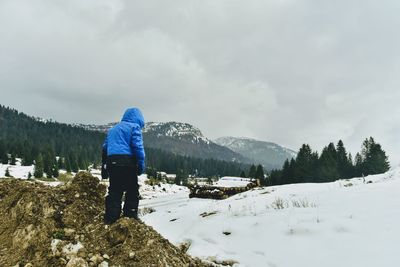 Rear view of person standing on snowcapped mountain against sky