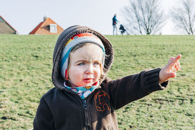 Cute girl pointing while standing on grassy field against sky