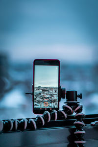 Close-up of mobile phone on railing against sky