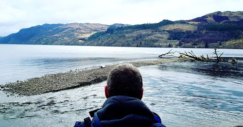 Rear view of man looking at sea against mountain range