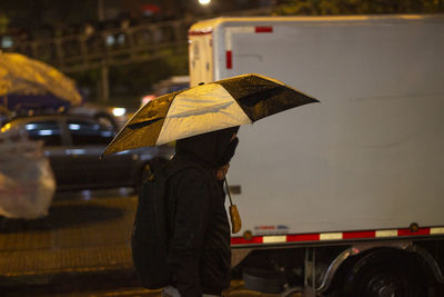 Side view of man standing with umbrella on wet road in rainy season