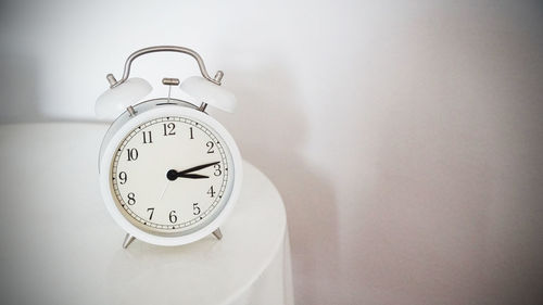 Close-up of alarm clock on table against wall at home