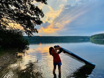 Rear view of man standing by lake against sky during sunset