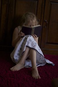 Girl holding book while sitting on bed at home