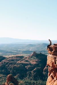 Man sitting on mountain against sky