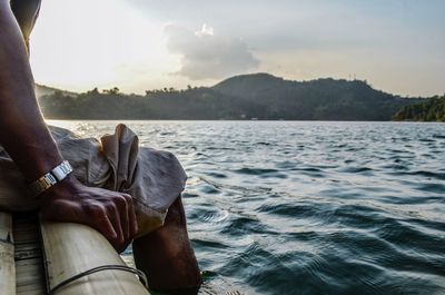 Low section of man sitting by sea against sky