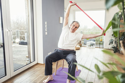 Senior man with resistance band exercising on chair at home