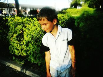 Smiling boy looking away while standing against plants