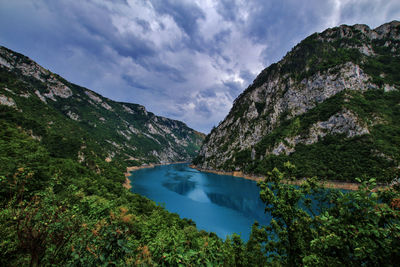 Scenic view of lake by mountains against cloudy sky