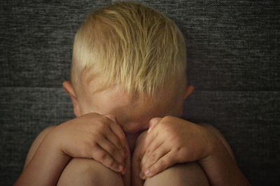 Close-up of sad shirtless boy sitting against wall at home