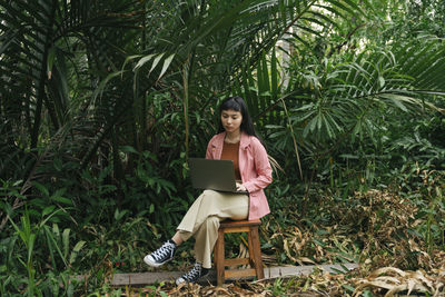 Young woman using mobile phone while sitting on tree