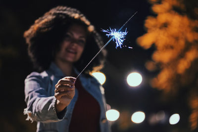 Smiling young woman holding sparkler at night