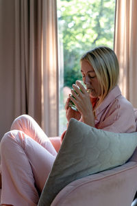 A blond woman in pink pajama sits in the pink armchair and sips mint tea.