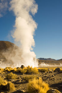 Geyser emitting smoke on landscape against clear blue sky