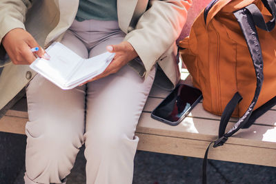 Cropped unrecognizable entrepreneur in suit sitting on bench and writing in planner while working remotely on sunny day in street restaurant