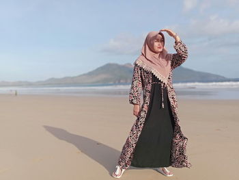 Woman in hijab standing at beach against sky