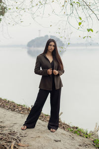 Full length portrait of young woman standing against tree