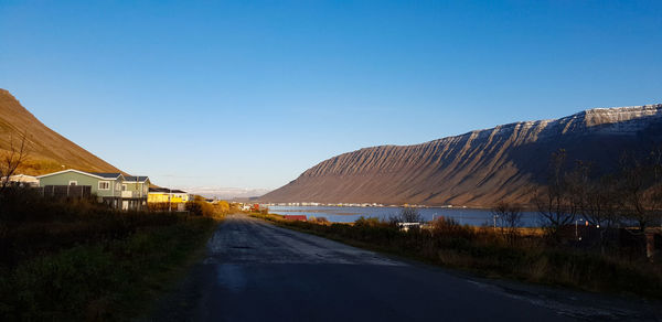 Road amidst buildings against clear blue sky