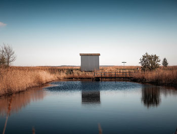 Hut by pond against clear sky