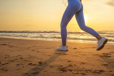 Low section of woman standing at beach against sky during sunset